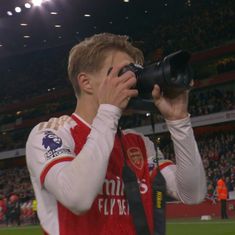 a man holding a camera up to his face in front of a stadium full of people