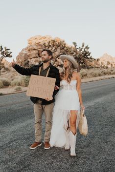 a man and woman standing in the middle of an empty road holding a cardboard sign