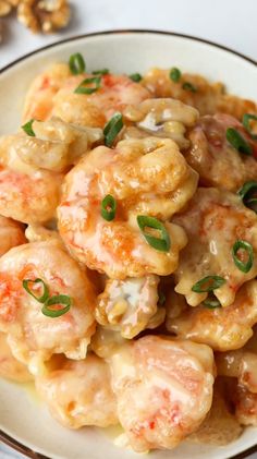 a white plate topped with shrimp covered in sauce and garnished with green onions