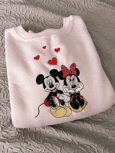 This Minnie and Mickey Valentines Embroidered Crewneck is perfect for celebrating the season of love! The crewneck features a classic fit silhouette and is made from a soft cotton fabric. The design is embroidered with a playful Minnie and Mickey Mouse design in bright red and pink colors, perfect for Valentine's Day. The neckline and cuffs feature ribbing for added comfort and a snug fit. This is the perfect crewneck for any Mickey and Minnie Mouse fan! Crewneck sizes are unisex.