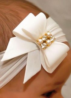 a close up of a baby's head wearing a white bow with pearls