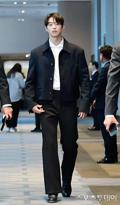 a man walking down a runway wearing a black suit and white shirt with his hands in his pockets