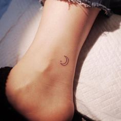 a woman's foot with a small crescent tattoo on her left ankle and the moon behind it