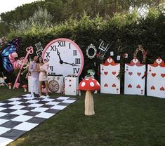 two people standing in front of a giant clock and checkered chess board on the lawn