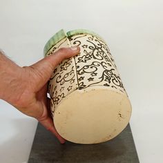 a hand is holding a decorative vase on a black and white base with green accents