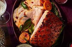 a turkey with herbs and oranges on a platter next to other dishes, glasses and utensils