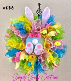 a colorful easter wreath with bunny ears and feet on it's head is displayed against a wall