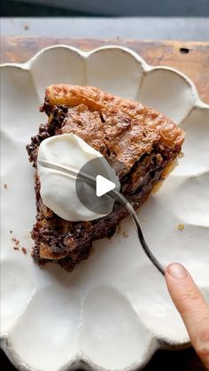 a piece of pie on a white plate with a spoon in it and someone's hand