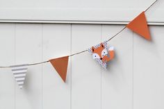 an orange and white paper fox garland hanging from a line on a wall next to a building