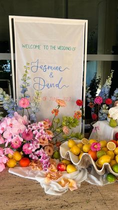 flowers and fruit are on display in front of a sign that reads welcome to the wedding of jasmine & david