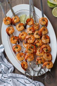 grilled shrimp skewers on a white plate with lime wedges next to them