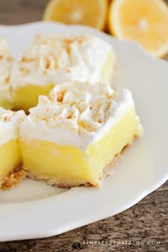 three slices of lemon meringue pie on a white plate with sliced lemons in the background