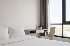 a bed with white sheets and pillows next to a window overlooking the cityscape