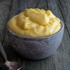 a bowl filled with yellow frosting on top of a wooden table next to a spoon