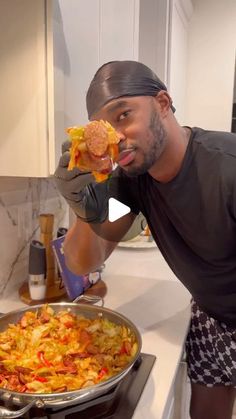 a man in black shirt holding up a piece of food next to a pan filled with vegetables