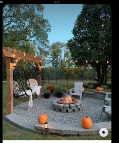 an outdoor fire pit surrounded by chairs and lights with pumpkins on the ground next to it