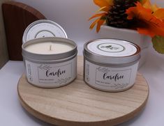 two candles sitting next to each other on a wooden tray with flowers in the background