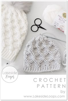 a crochet hat, yarn and scissors on a white table with balls of yarn