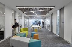 an office with colorful chairs and tables in the center, while people are walking around