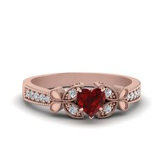 a heart shaped red diamond ring with white diamonds on the band and side stones in 18k rose gold