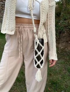 a woman in white shirt and beige pants holding a black bag with tassels on it