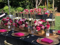 the table is set with pink flowers and gold place settings for an outdoor wedding reception