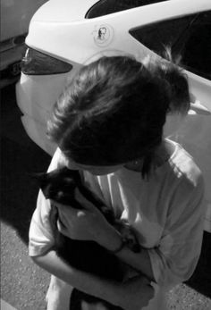 a woman holding a cat in her arms next to a white car on the street