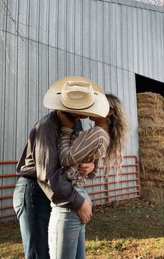 a man and woman kissing in front of a barn with hay bales behind them