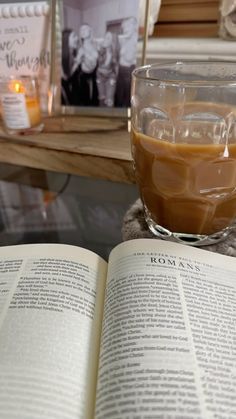 an open book sitting on top of a table next to a glass filled with liquid