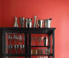 an assortment of wine glasses and silverware on a black shelf against a red wall