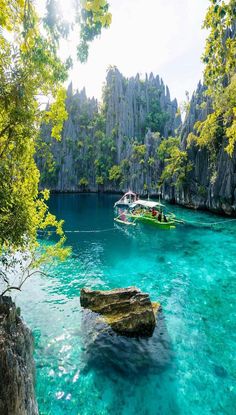 boats floating in the blue water near some rocks and green trees, surrounded by cliffs