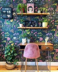 a desk with a pink chair in front of a wallpapered wall and shelves