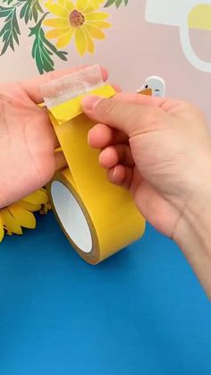 someone is holding a roll of yellow tape in front of a wall with flowers on it