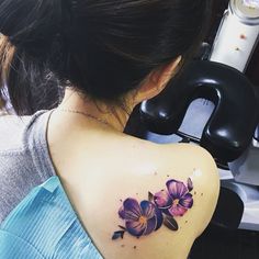 a woman's back shoulder tattoo with purple flowers