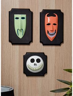 three halloween masks are hanging on the wall next to a potted plant and vase