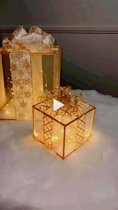 three gold gift boxes with lights on them sitting in the snow next to each other