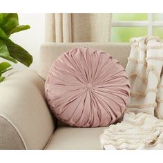 a pink pillow sitting on top of a white couch next to a green potted plant