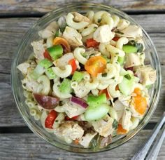 a glass bowl filled with pasta salad on top of a wooden table