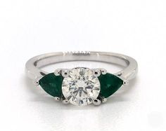 a diamond and emerald ring on a white surface with the center stone surrounded by three green stones