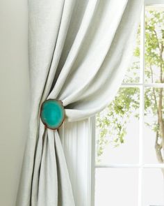 a curtain with a turquoise ring hanging on it's side in front of a window