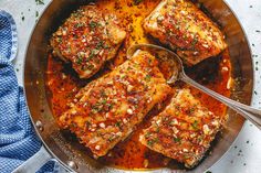 four pieces of meat in a pan with sauce and seasoning on the side next to a blue towel