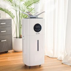 a white air purifier sitting on top of a wooden floor next to a plant