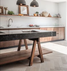 a modern kitchen with marble counter tops and wooden shelves on the wall, along with two hanging lights