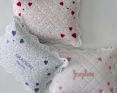 two pillows with hearts on them sitting next to each other in front of a white wall