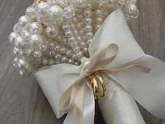 a bunch of pearls tied to a white ribbon on top of a wooden table next to a ring