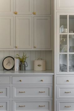 a kitchen with white cabinets and gold pulls on the cupboards, along with a clock