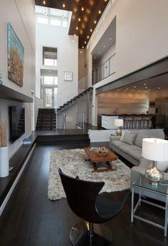 a large living room with high ceilings and hardwood floors is furnished with modern furniture, as well as a staircase leading up to the second floor