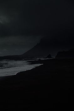 a black and white photo of the ocean at night with dark clouds in the sky