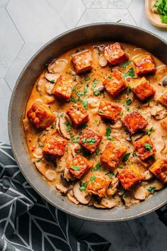 a skillet filled with meat and vegetables on top of a marble counter next to a cutting board