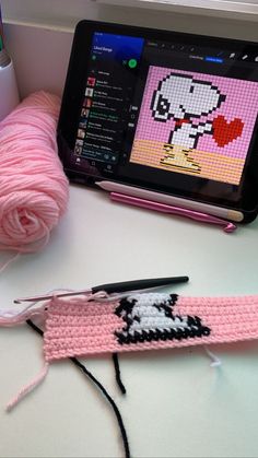 a tablet computer sitting on top of a table next to a pink crocheted object